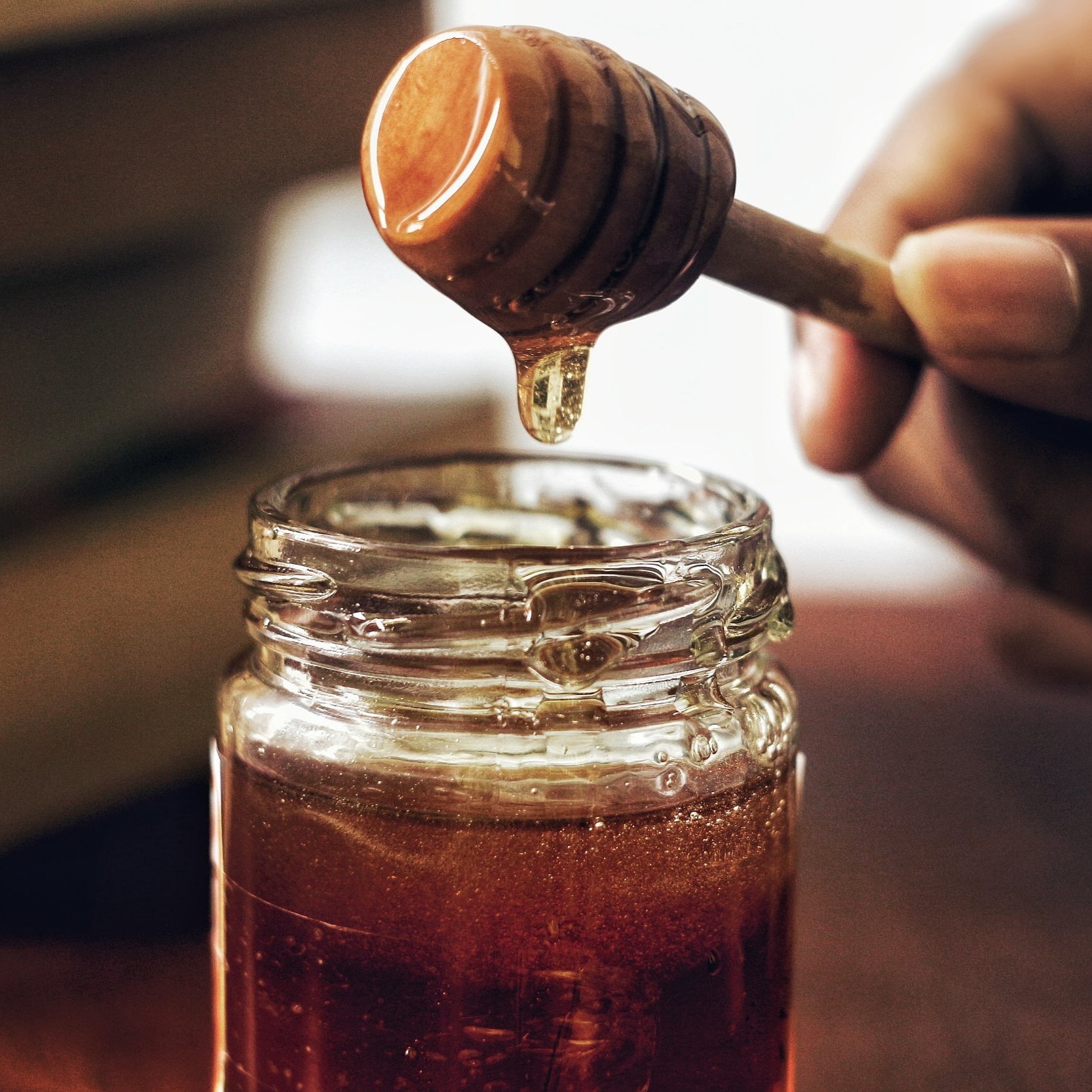 Close-up of a honey dipper dripping golden honey into a glass jar, highlighting the rich texture and color of natural honey.